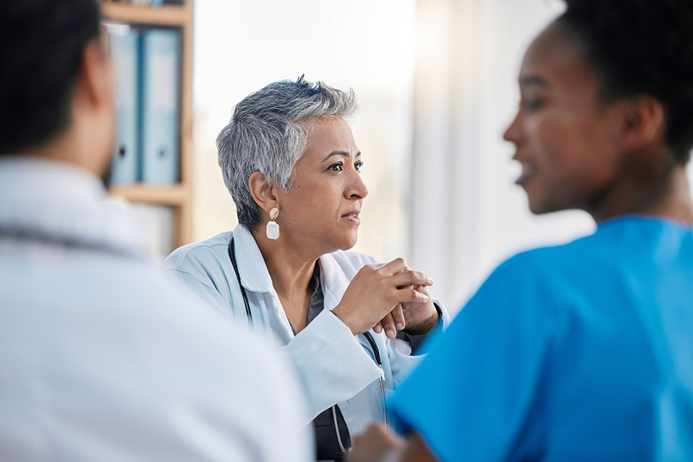 A woman with short grey hair speaks with two medical professionals